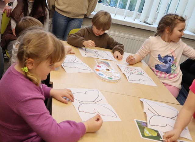 dzieci siedzą przy stołach i malują na kartkach