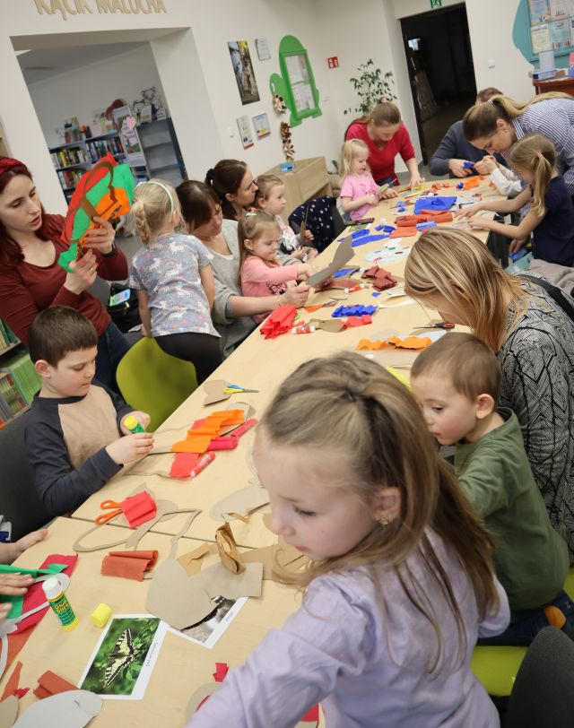 dzieci z rodzicami siedzą przy stołach i malują na kartkach