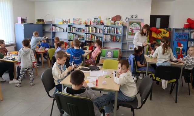 dzieci przy stolikach rysują i wycinają z kolorowego papieru i rolek po papierze toaletowym, w tle regały z książkami