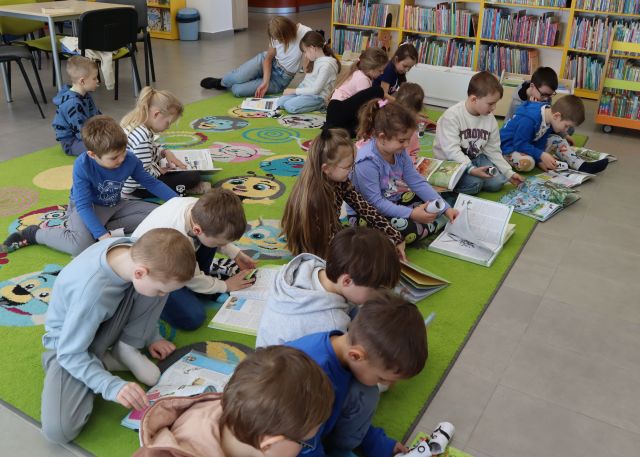 dzieci siedzą na kolorowym dywanie i przeglądają książki