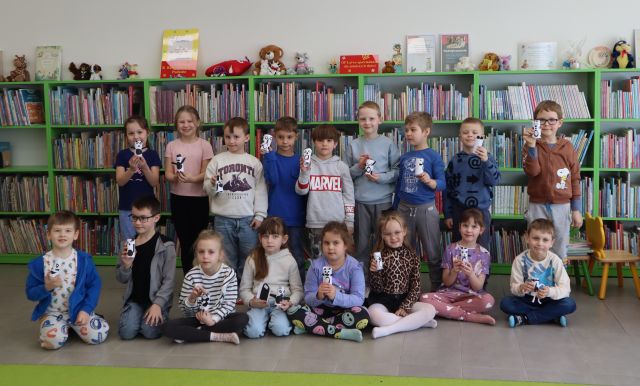 grupa przedszkolaków pozuje do zdjęcia, w tle regały z książkami