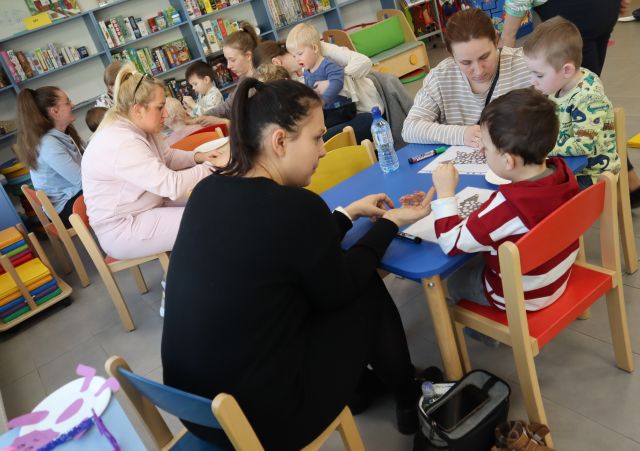 dzieci z mamami siedzą przy stolikach i malują na kartkach