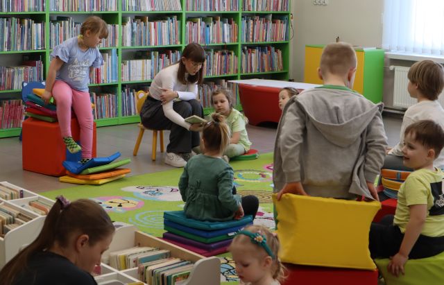 dzieci z bibliotekarką siędzą na kolorowym dywanie