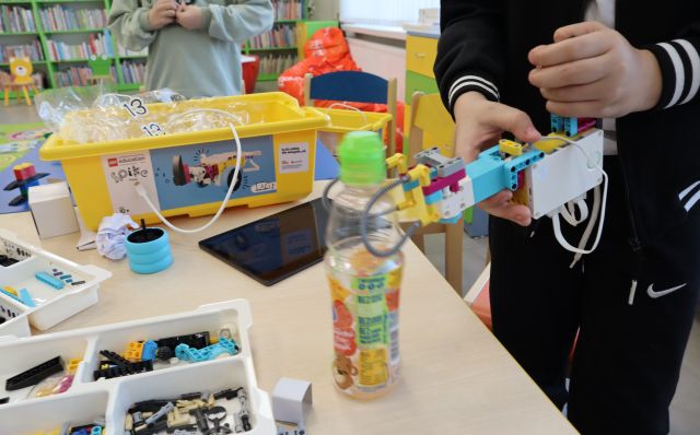 chłopiec prezentuje budowlę z kolcków LEGO, na stole pudło z klockami