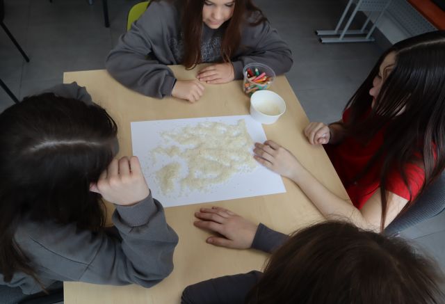 4 osoby siedzą przy stole i sypią ryż na kartkę