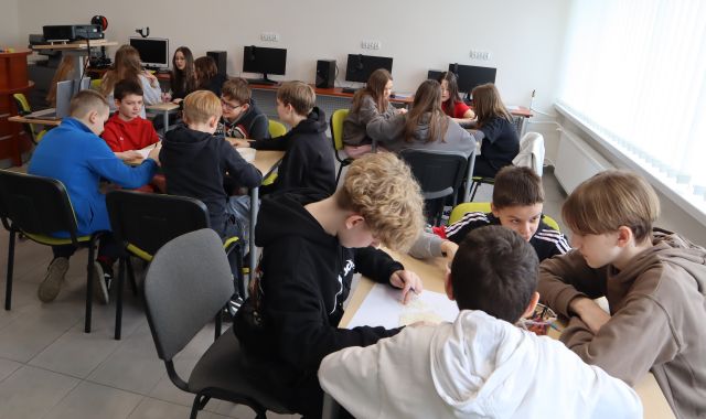 młodzież siedzi przy stołach w sali komputerowej