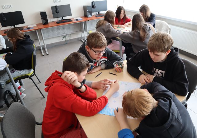 młodzież siedzi przy stołach i rysuje