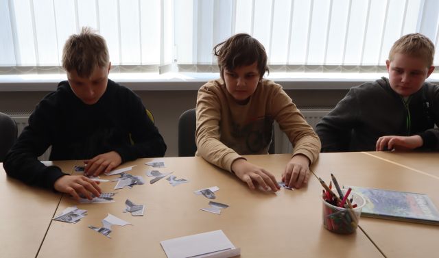 młodzież siedzi przy stołąch i układa puzle