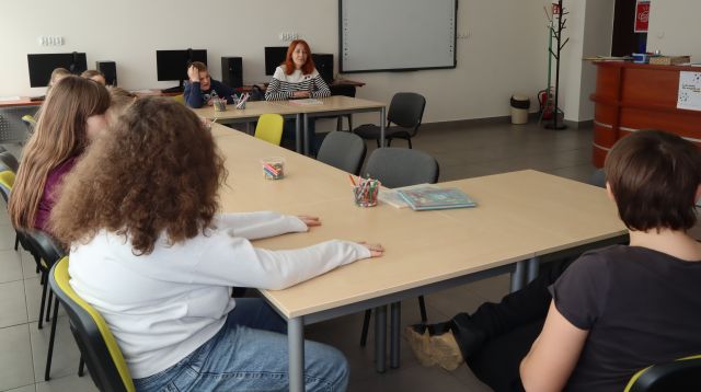 młodzież z nauczycielką siedzą przy połączonych stołach