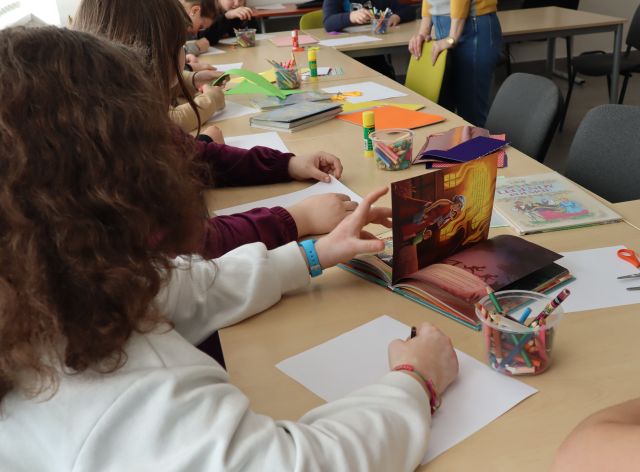 młodzież siedzi przy połączonych stołach, na stołach leżą kartki i książki