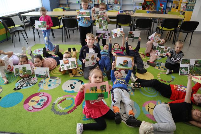 przedszkolaki siedzą na dywanie i prezentują swoje prace plastyczne