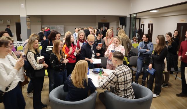 tłum ludzi czeka w kolejce po autograf, przy stoliku siedzi tyłęm mężczyzna i kobieta