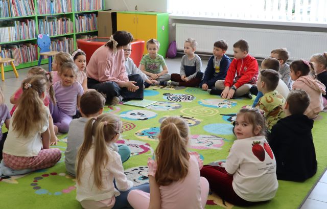 przedszkolaki siedzą z bibliotekarka na dywanie