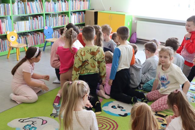 przedszkolaki siedzą i klęczą na dywanie