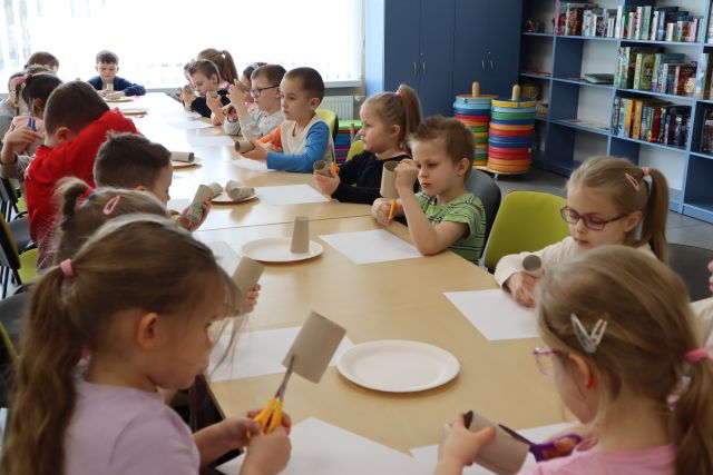 przedszkolaki siedzą przy stolikach, przed nimi kartki i papierowe talerzyki