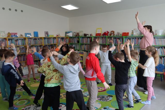 przedszkolaki stoją na dywanie, w tle regały z książkami