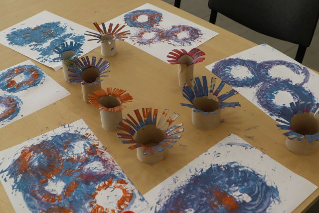 na stole pokolorowane kartki, obok rolki po papierze toaletowym umaczane w farbie