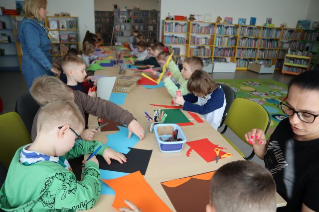 przedszkolaki siedzą przy stolikach, wycianją i kleją