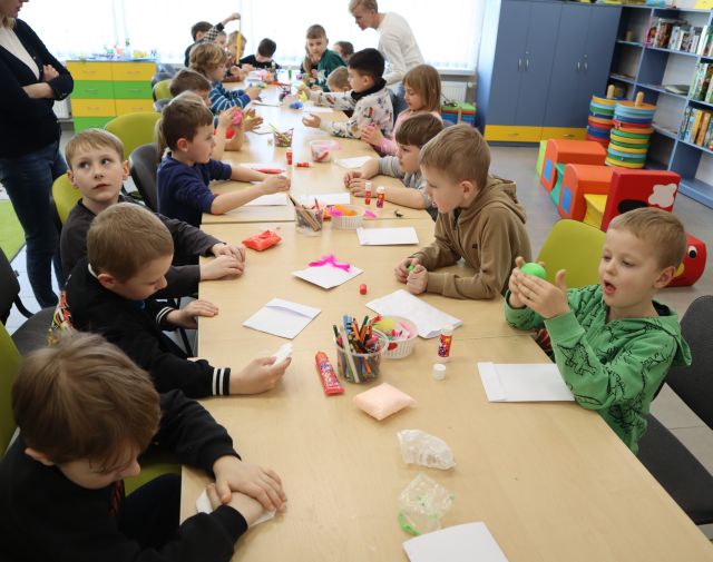 dzieci siedzą przy połączonych stołach i lepią z plasteliny