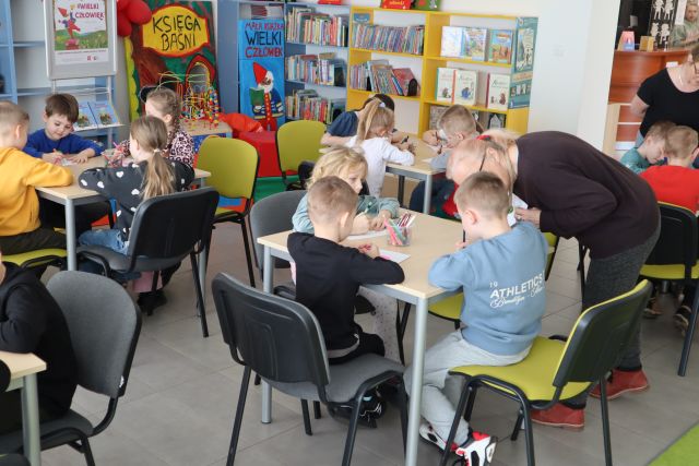 dzieci siedzą przy stołach i rysują na kartkach