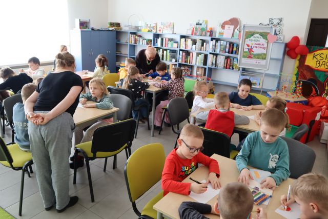 dzieci siedzą przy stołach i rysują na kartkach