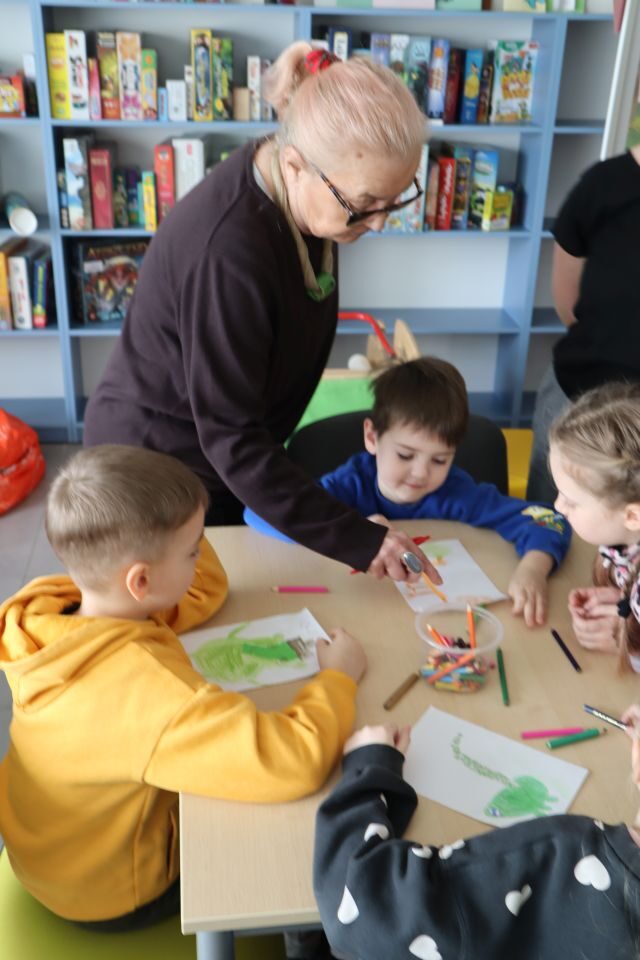 dzieci rysują na kartkach, przy nich stoi kobieta