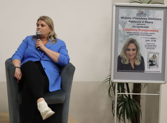 na fotelu siedzi kobieta z mikrofonem, obok plakat promujący spotkanie
