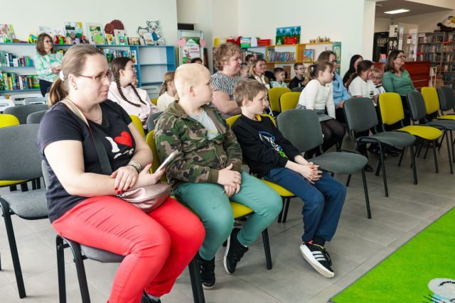 dzieci i osoby dorosłe siedzą na krzesłach