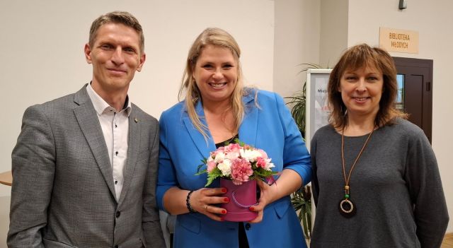 burmistrz i dyrektorka biblioteki pozują do zdjęcia z Romanowską trzymającą w dłoniach kwiaty