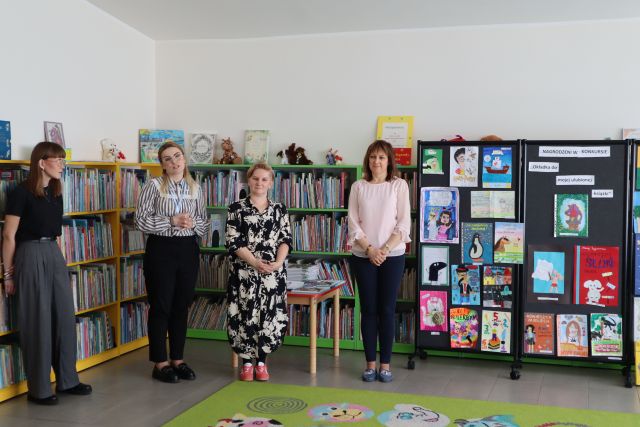 4 kobiety stoją na tle regałów z książkami, z prawej strony tablica z pracami plastycznymi