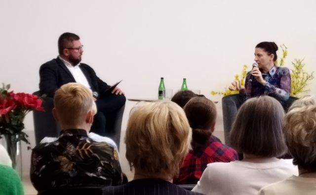 na scenie przy stole na fotelach siedzi mężczyzna i kobieta przed publicznością