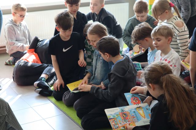 dzieci siedzą na dywanie i przeglądają książki