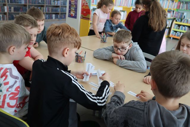 dzieci siedzą przy stołach, w dłoniach trzymają karteczki