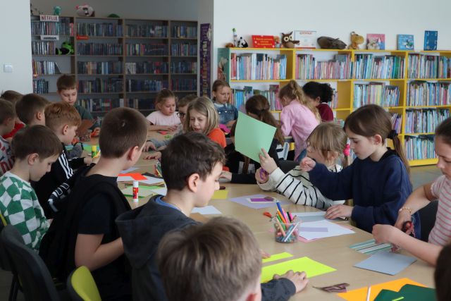 dzieci siedzą przy stołach, na stołach leżą kartki i przybory do malowania