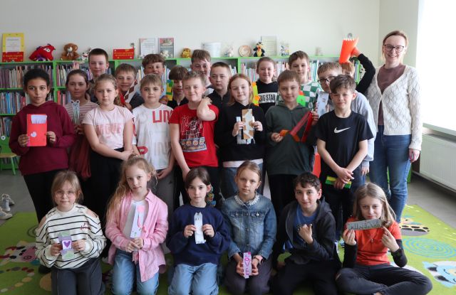 dzieci pozują do zdjęcia z zakładkami, w tle regały z książkami