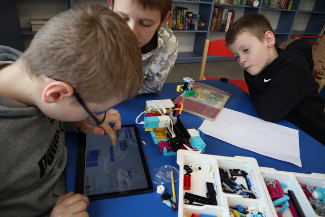 chłopiec pisze na tablecie, dwóch chłopców siedzi przy stoliku z klockami LEGO