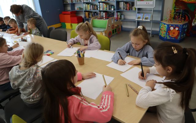 dzieci siedzą przy stolikach i malują na kartkach