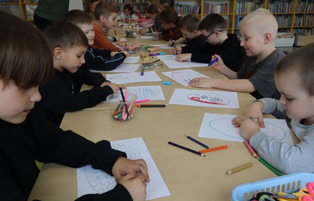dzieci siedzą przy stolikach i malują na kartkach