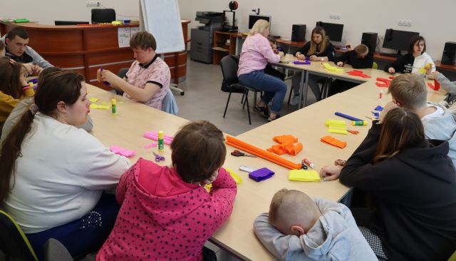 młodzież z opiekunami siedzą przy stołach, na stołach bibuła, nożyczki kleje
