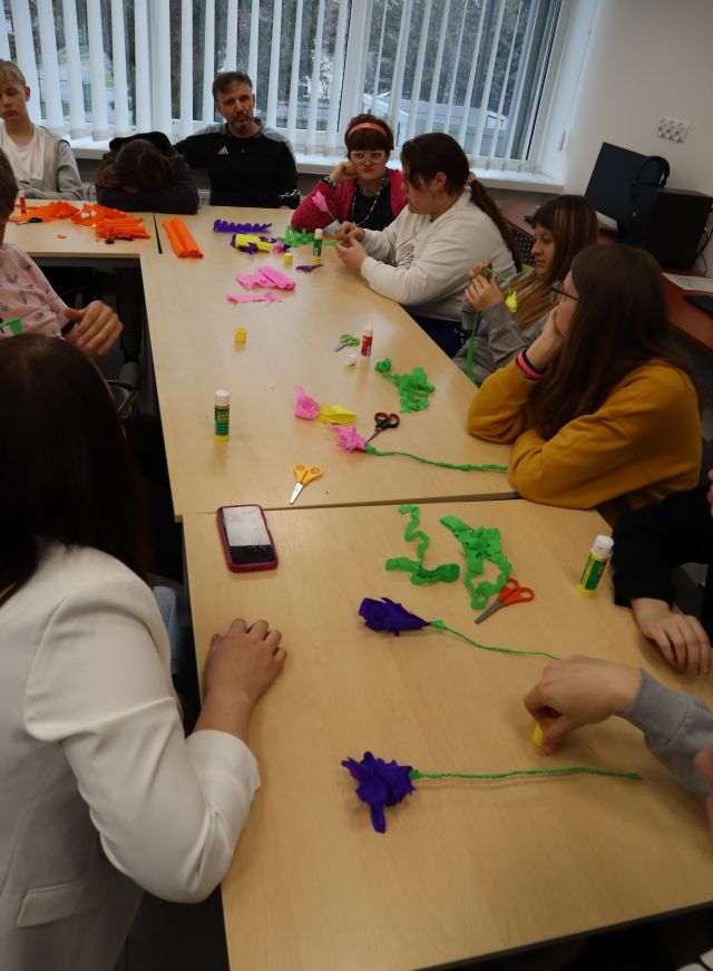 na stołach kwiaty z bibuły, na zdjęciu widać ręce uczestników warsztatów