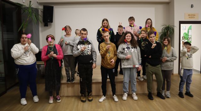 blisko 20 młodych ludzi pozuje do zdjęcia, w rękach trzyma kwiaty z bibuły