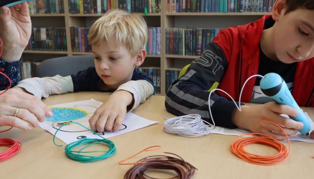 dwóch chłopców maluje długopisami 3D, w tle regały z książkami