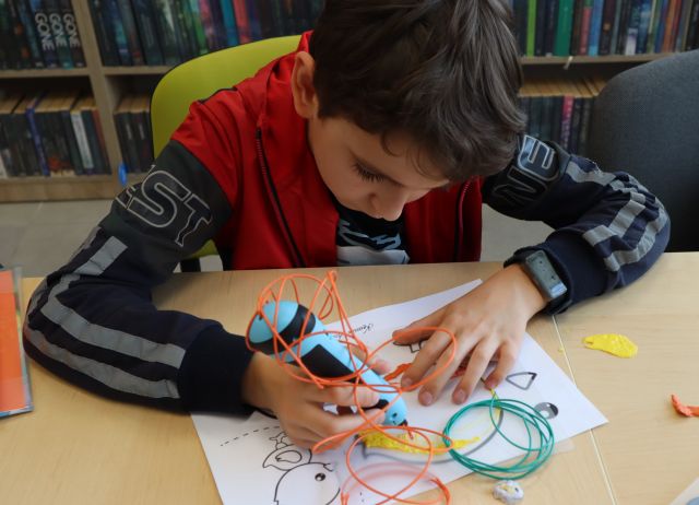 chłopiec trzyma w, na kartce kolorowe linie z filamentów dłoniach długopis 3D