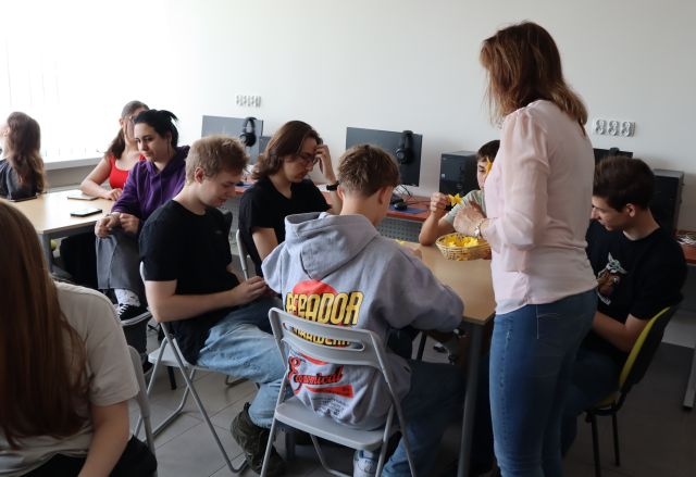 dyrektorka biblioteki z koszyczkiem z papierowymi żonkilami, przy stolikach w sali komputerowej siedzi młodzież