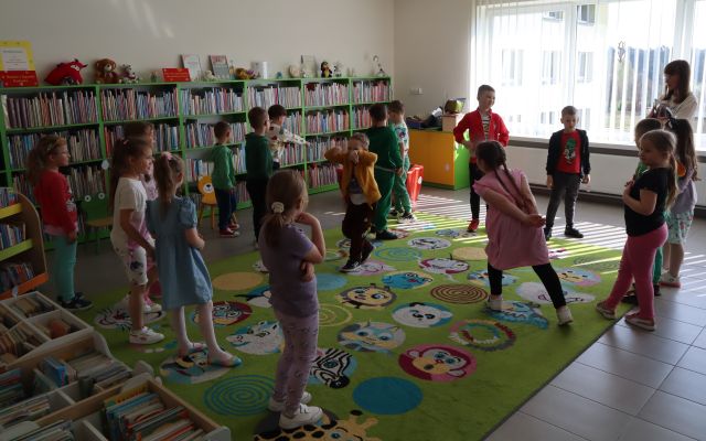 przedszkolaki stoją na kolorowym dywanie i podłodze, w tle regały z książkami