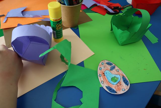 na stoliku papierowy koszyczek, pisanki z papieru i kolorowe kartki