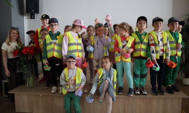 Przedszkolaki w żółtych kamizelkach i z przypiętymi papierowymi żonkilami pozują do zdjęcia