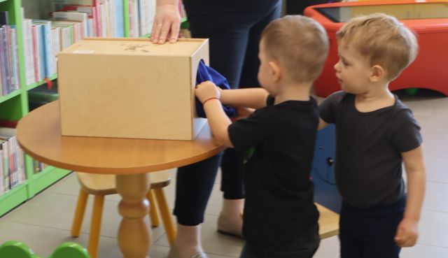 chłopiec trzyma dłonie w skrzynce z otworem, za nim stoi drugi chłopiec