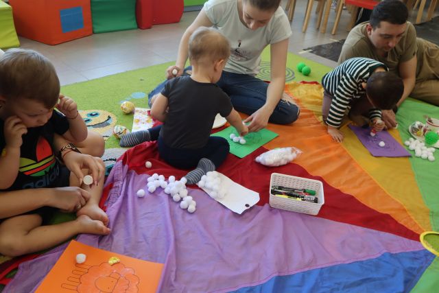 dzieci z rodzicami naklejaja białe pomponiki na kartkę