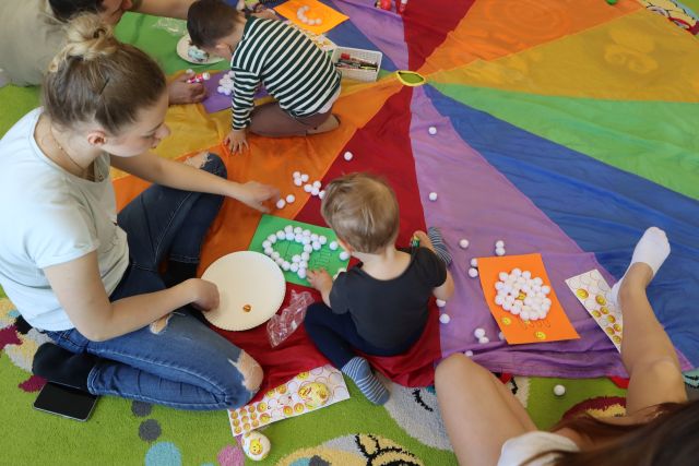 dzieci z rodzicami naklejają pomponiki na kartce